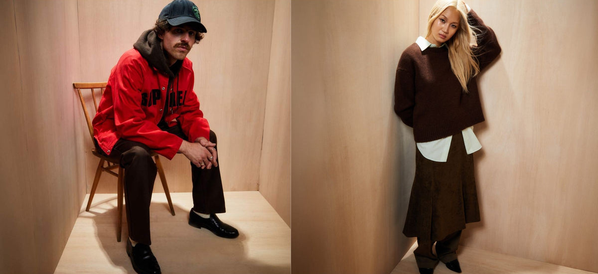 A split-screen lifestyle image featuring two models in a minimalist wood-paneled room. On the left, a man wearing a red jacket, black trousers, and a cap sits on a wooden chair.